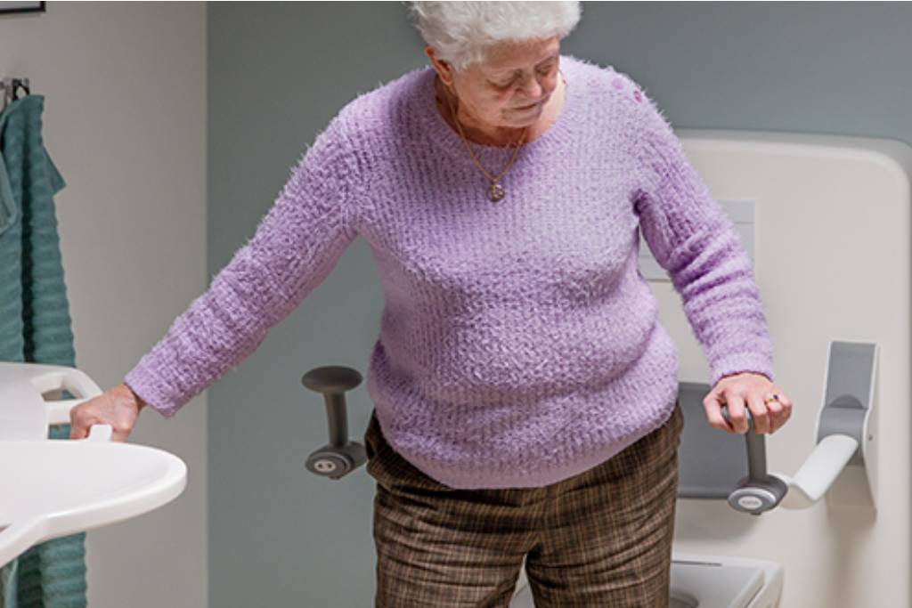 hot to care for aging parents showing elderly lady grabbing support bars in bathroom